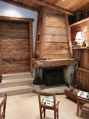 A rustic wooden interior with a stone fireplace, wooden benches, and a shelf with various items.