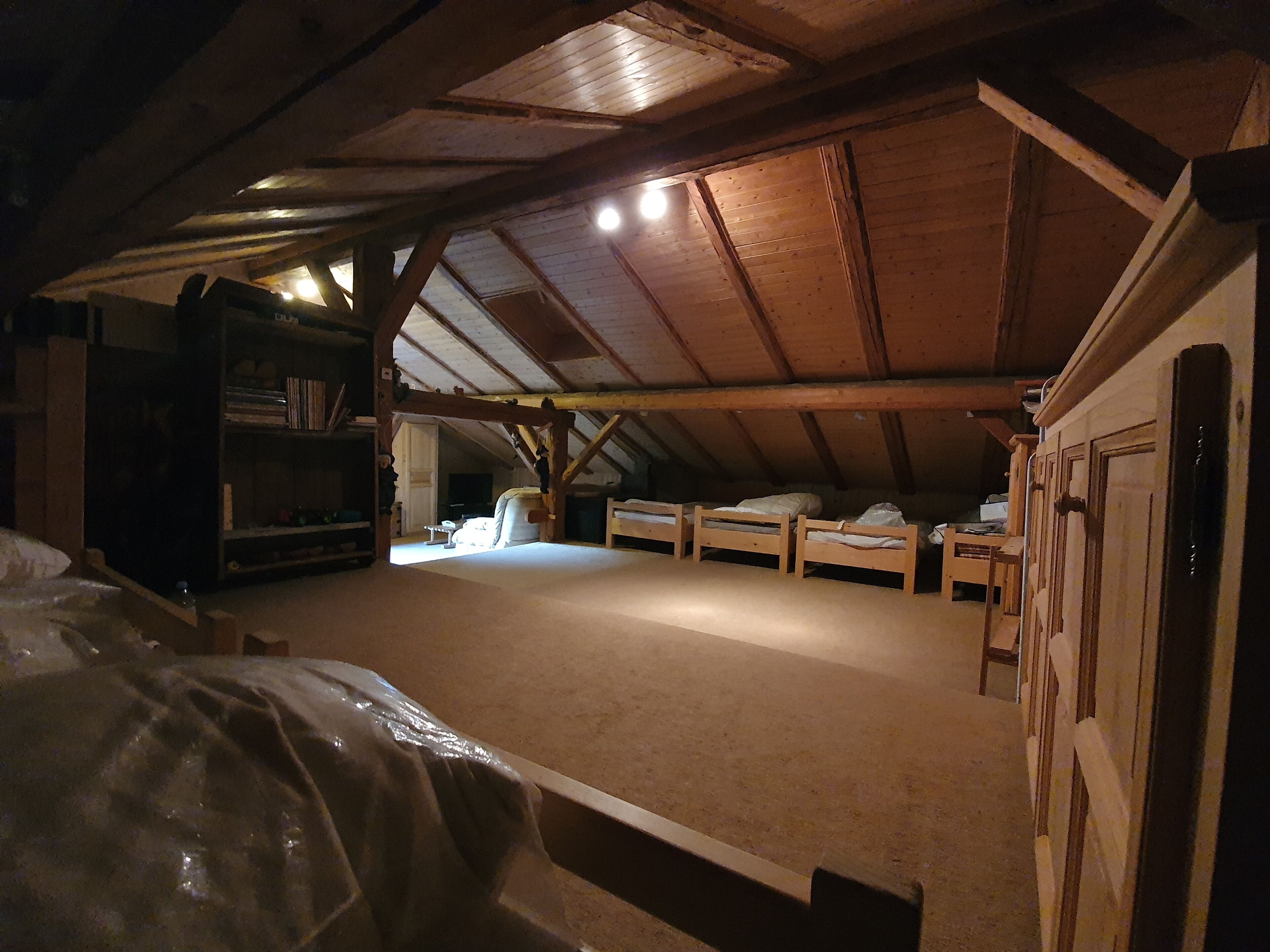 A high-ceilinged attic room with wooden beams, a bookshelf, and three bunk beds.