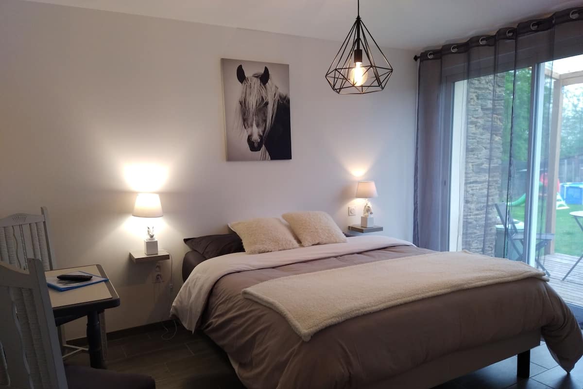A bedroom with a bed, two bedside lamps, a nightstand, a chair, a desk, a picture of a horse, and a window with curtains.