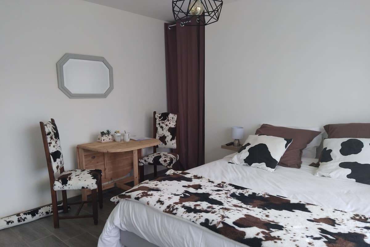 A bedroom with a bed, a desk, a chair, a mirror, and a nightstand with a lamp.
