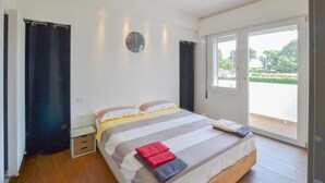 Ein modernes Schlafzimmer mit einem großen Bett, einem Nachttisch, einer Wanduhr und Blick ins Freie durch eine Schiebetür.