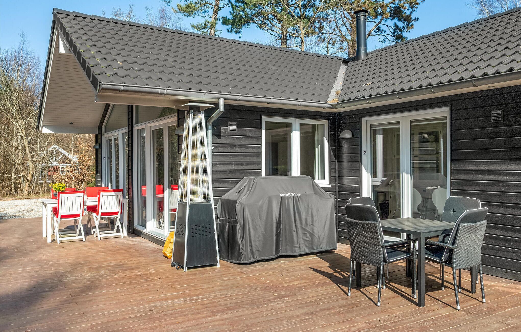 Een overdekt terras buiten met een barbecue, eettafel en stoelen.