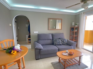 A living room with a grey sofa, a wooden coffee table, and a dining table with a bouquet of flowers.