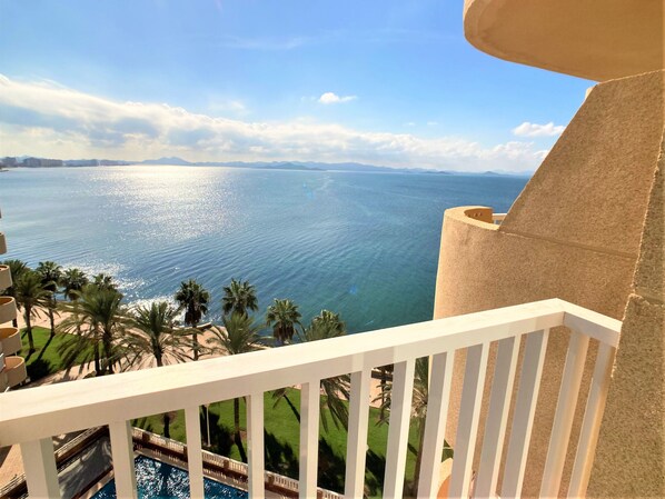 Un balcón con vista al mar, palmeras y una piscina.