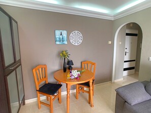 A dining area with a round wooden table, two wooden chairs, a vase with flowers, and wall art.