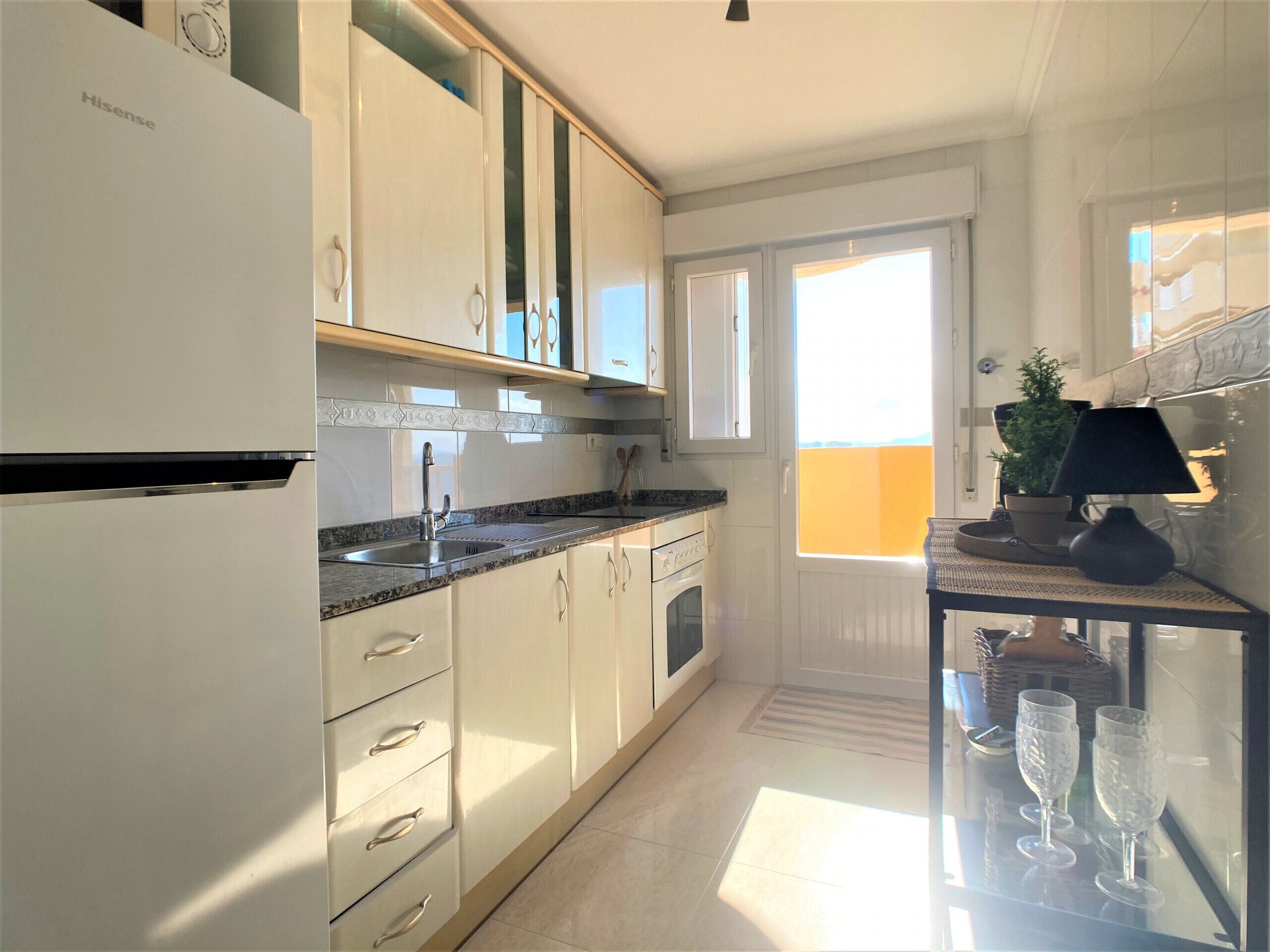 A modern kitchen with white cabinetry, a stainless steel sink, and a built-in oven. There is a window providing natural light and a view of the outdoors.