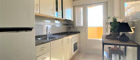 A modern kitchen with white cabinetry, a stainless steel sink, and a built-in oven. There is a window providing natural light and a view of the outdoors.