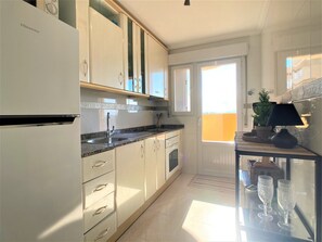 A modern kitchen with white cabinetry, a stainless steel sink, and a built-in oven. There is a window providing natural light and a view of the outdoors.