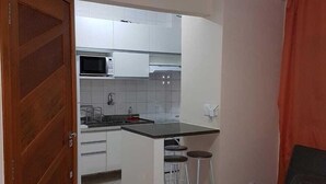 Eine kompakte Küche mit weißen Schränken, einer Mikrowelle und einem Deckenventilator. Im Wohnbereich befindet sich ein kleiner Barhocker und ein Sofa.