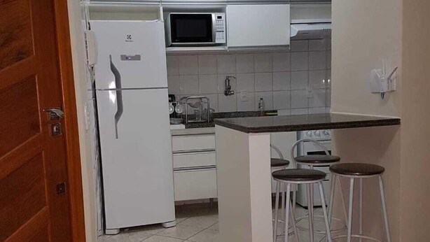 Eine Küche mit weißen Schränken, einem Kühlschrank, einer Mikrowelle und einer kleinen Bar mit Hockern.
