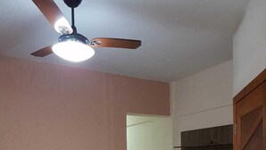 Ein Wohnzimmer mit Deckenventilator, einem an der Wand montierten Flachbildfernseher und einer Gruppe dunkler Ottomanen an der Wand.