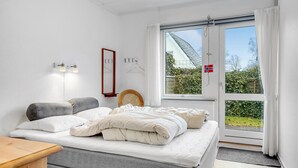 A bedroom with a bed, a bedside table, a mirror, and a window with curtains.