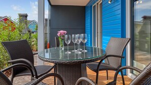 A glass-top table with wicker chairs and a vase of flowers on a balcony with blue siding. - Cozy home in Süssau/Ostsee with sauna (Süssau/Ostsee)