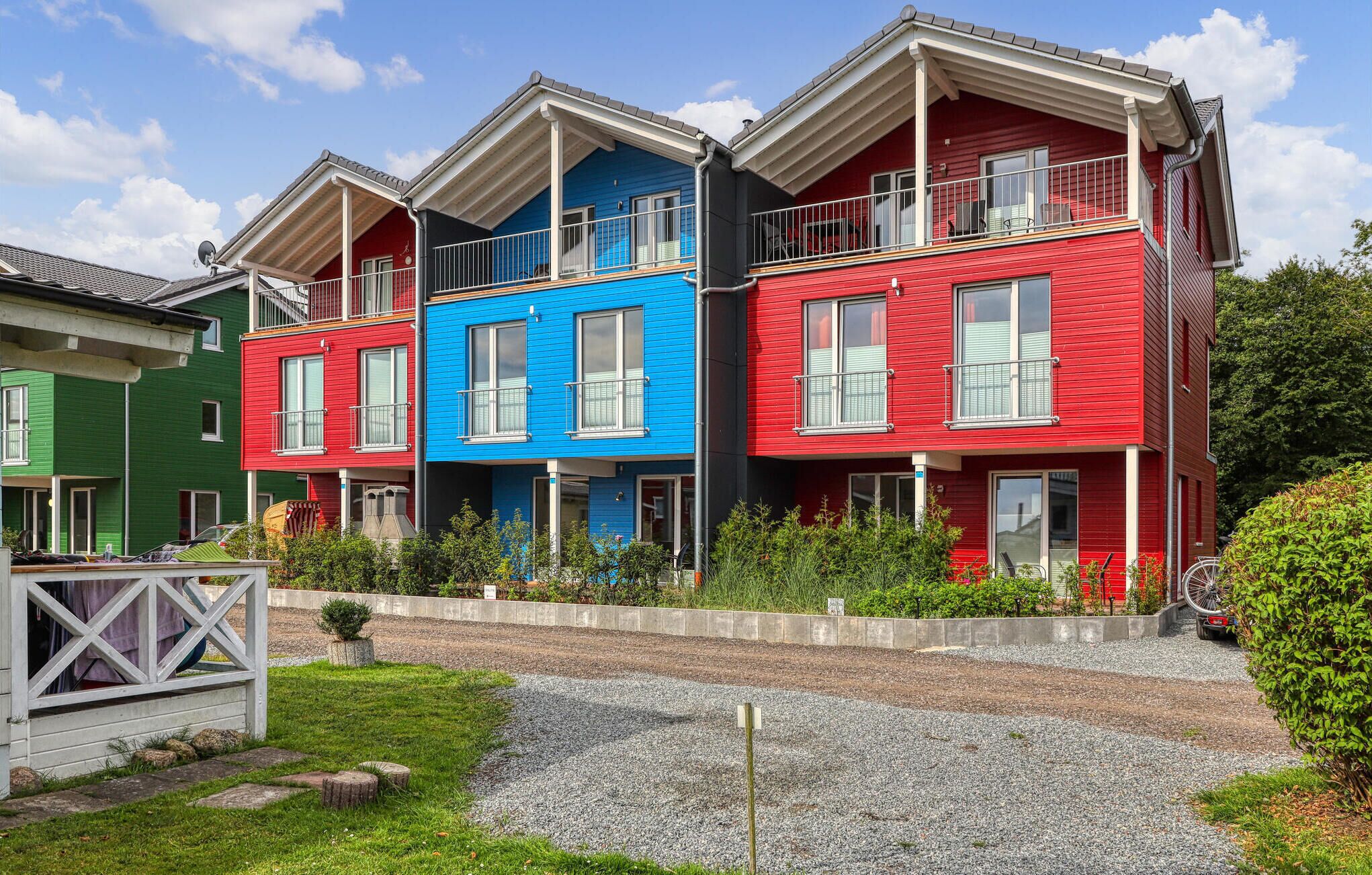 Farverige huse med balkoner, en grussti og et lille haveområde.