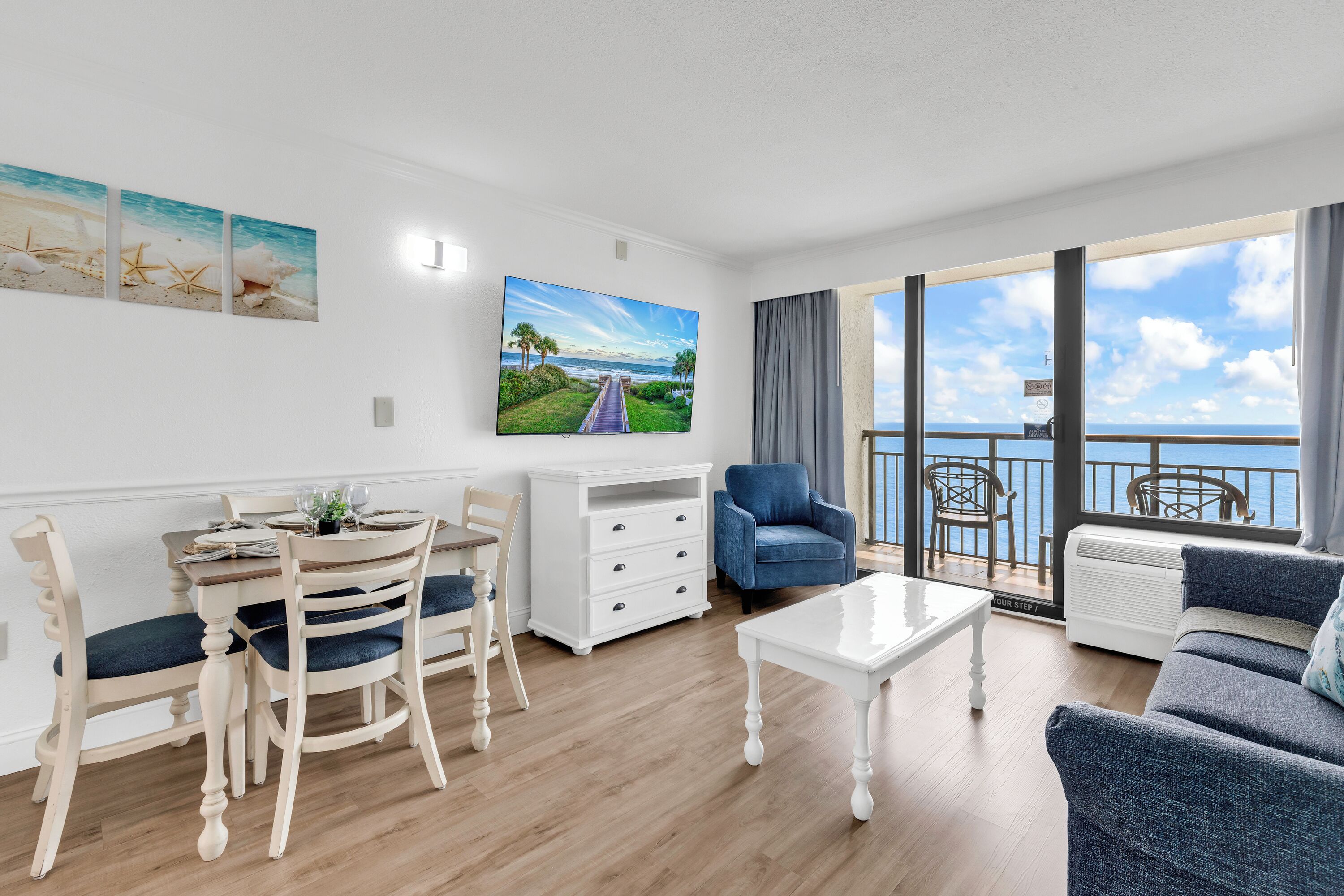A living room with a dining area, a sofa, a TV, and a balcony with a view.