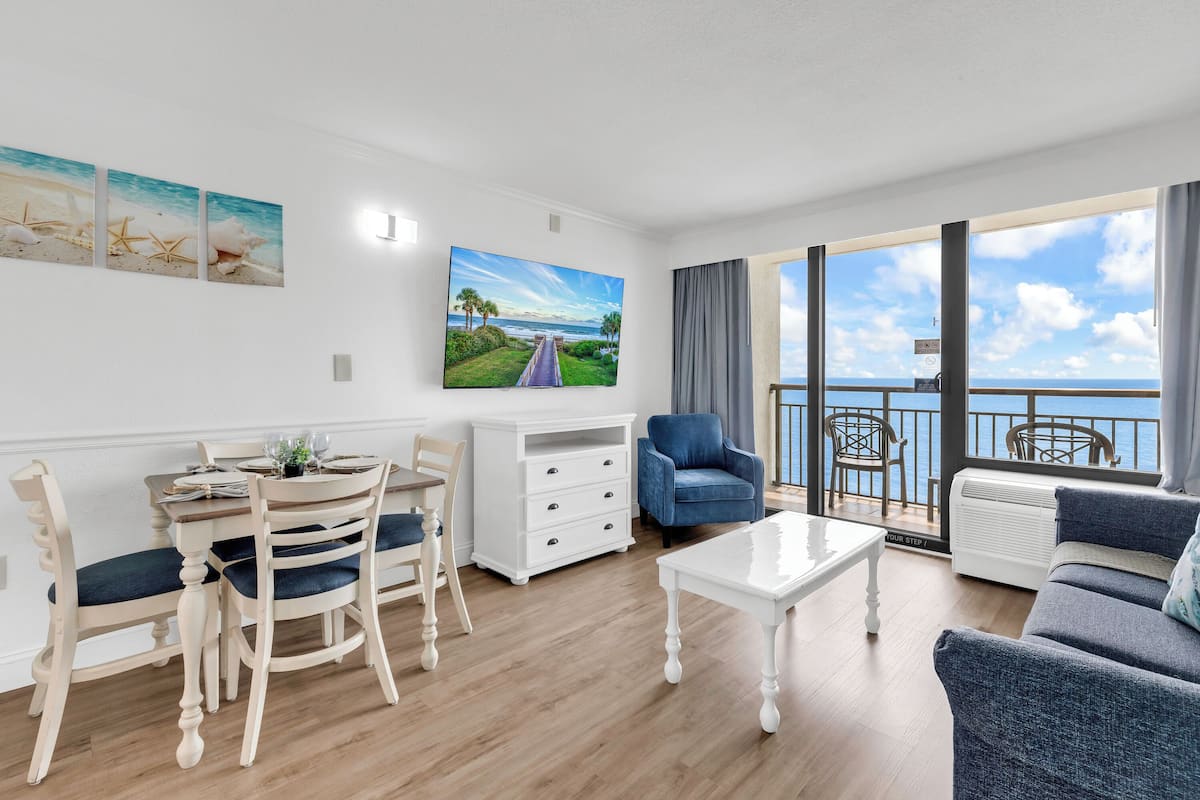 Ein Wohnzimmer mit Essbereich, einer Couch, einem Fernseher und einem Balkon mit Blick.