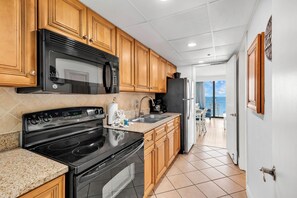 A kitchen with wooden cabinets, a black stove, a microwave, and a refrigerator. - Beach-front Condos Located in the Caribbean Resort with Pool and Lazy River (Myrtle Beach)
