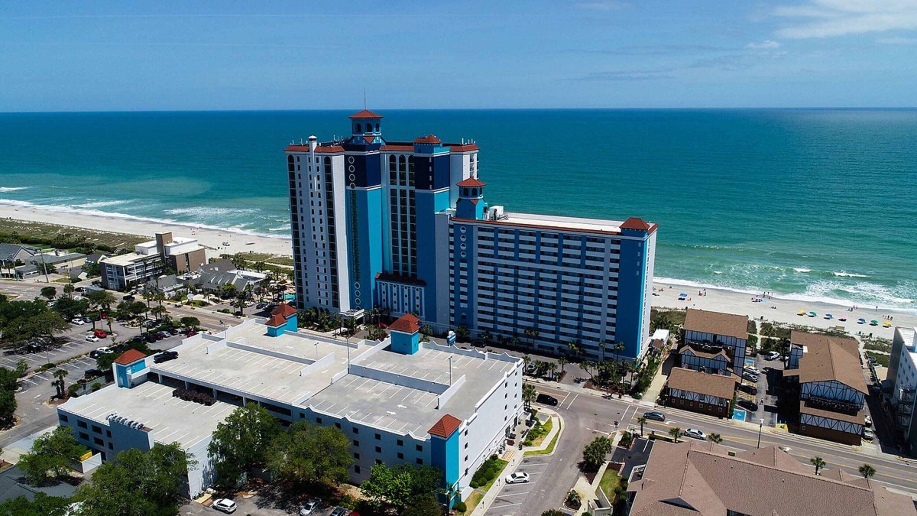 A high-rise hotel with multiple floors, a prominent tower, and a beach view.