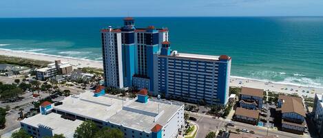 A high-rise hotel with multiple floors, a prominent tower, and a beach view.