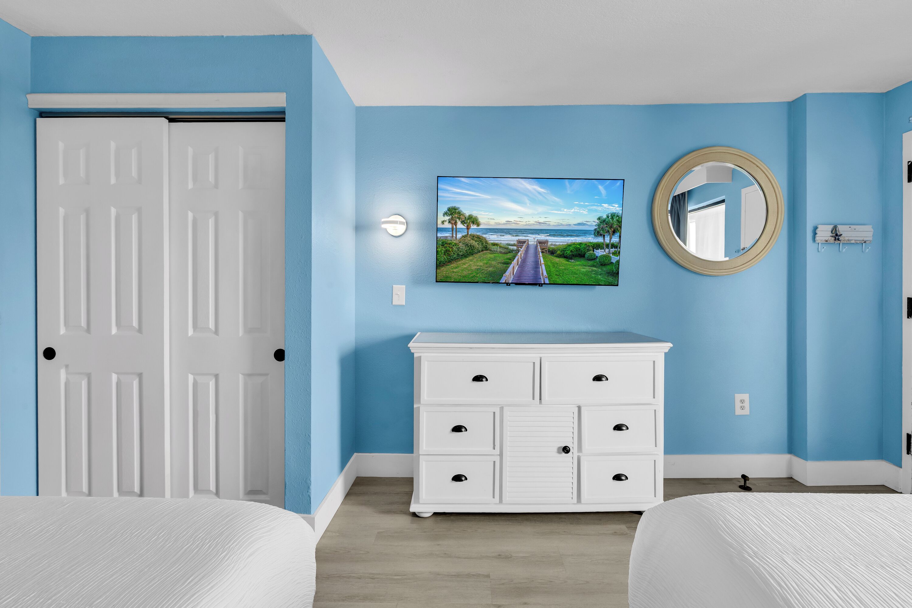 A bedroom with two beds, a white dresser, a television, and a wall-mounted mirror.