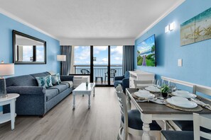 A room with a balcony, a dining table set with plates and glasses, a sofa, and a TV. - Beach-front Condos Located in the Caribbean Resort with Pool and Lazy River (Myrtle Beach)