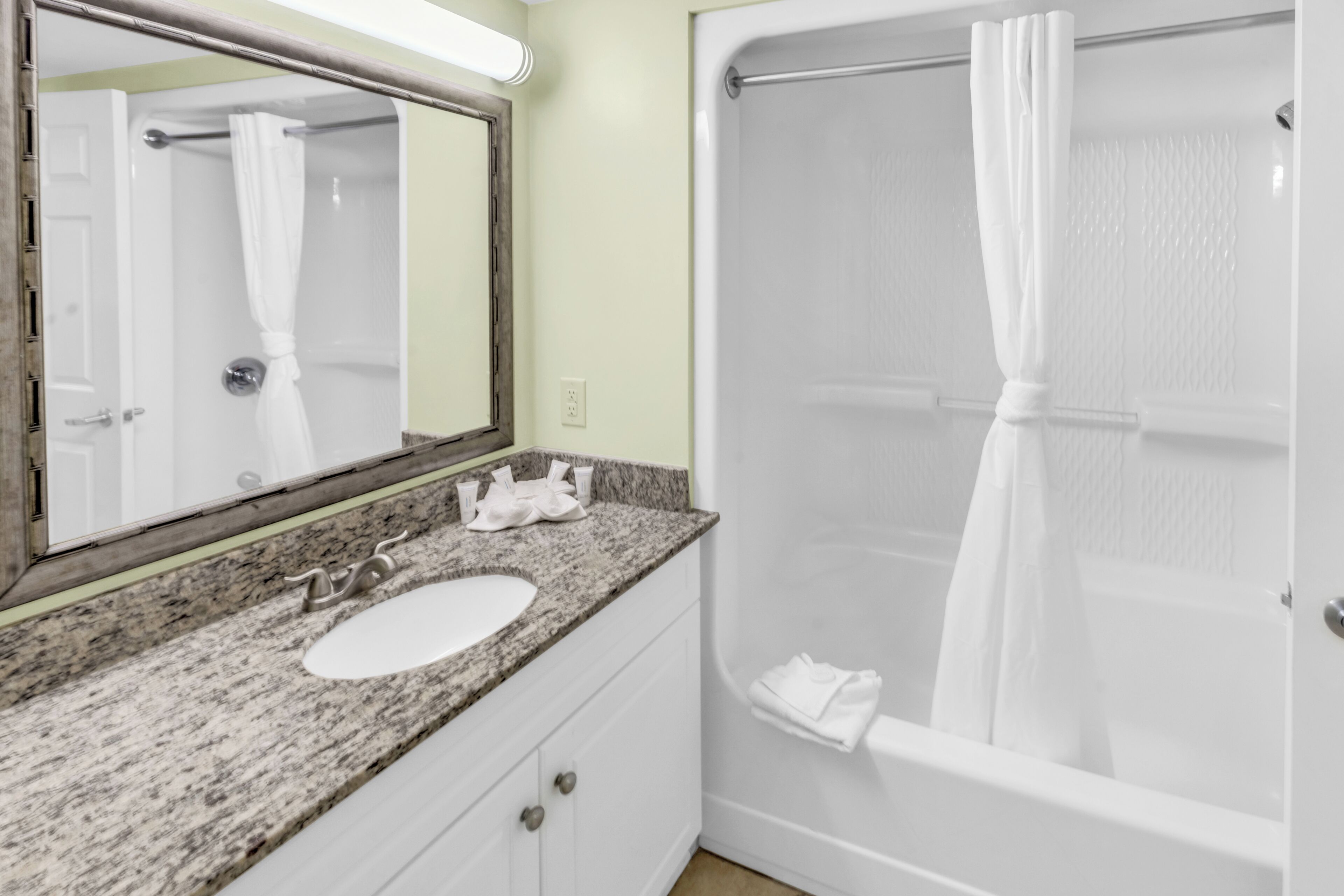 A bathroom with a granite countertop, a white sink, a mirror, a shower with a white curtain, and a towel rack.