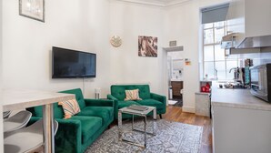 A modern living room with a green sofa set, a flat-screen TV, and a small table.