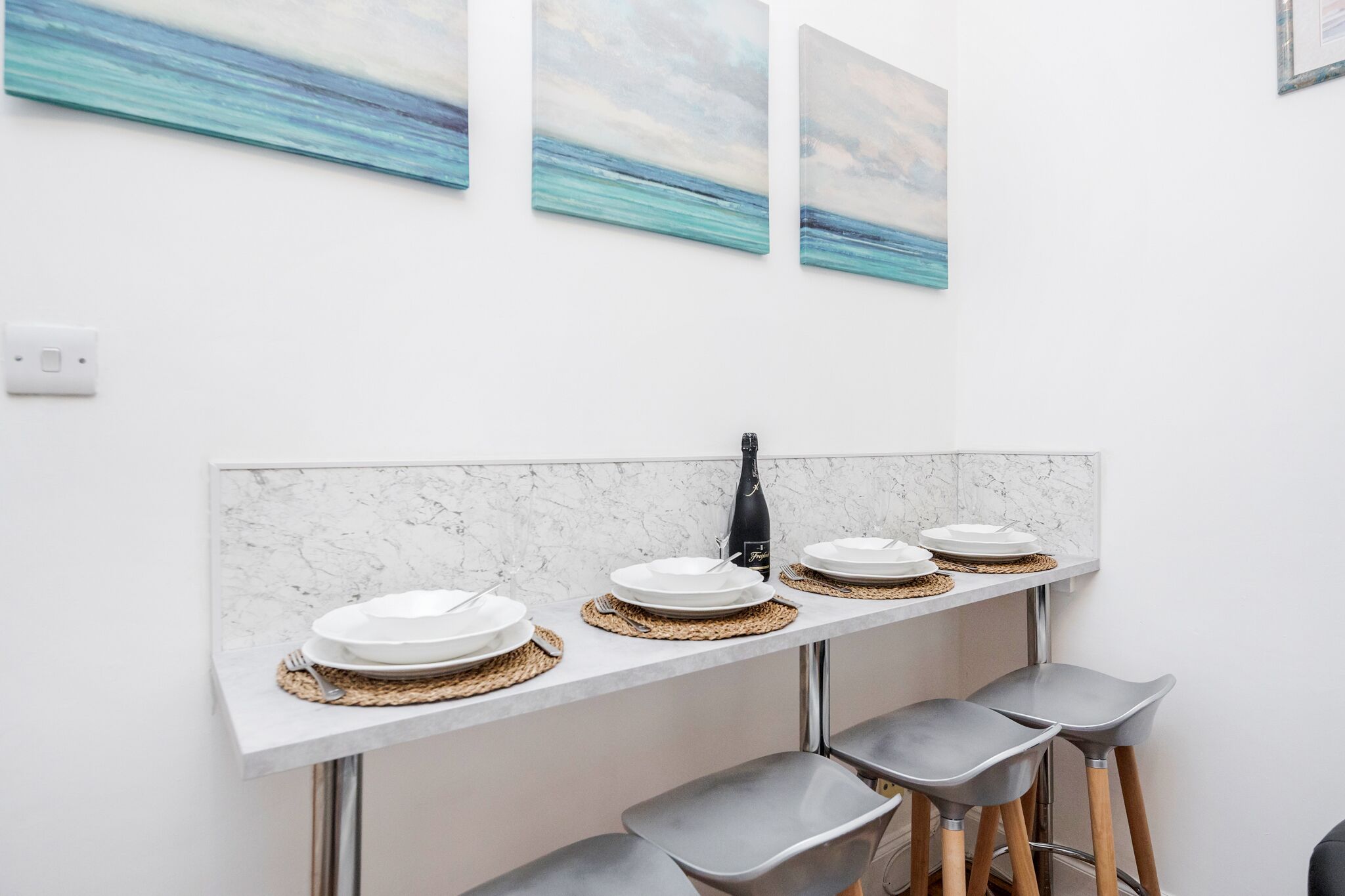 A modern kitchen with a marble countertop, a wine bottle, and three plates.