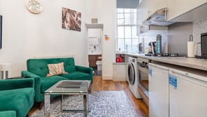 A modern apartment with a green sofa, a small table, a washing machine, and a kitchen area.