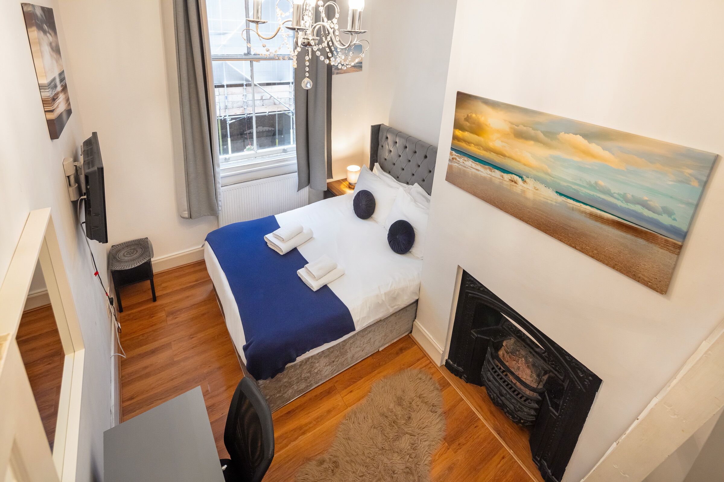 Une chambre à coucher avec un lit, une cheminée, une fenêtre avec des rideaux, un lustre et un tableau au mur.