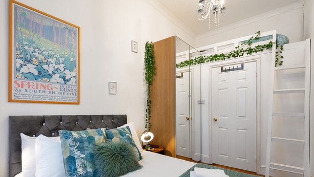 A bedroom with a bed, a nightstand, a mirror, a wardrobe, and a poster on the wall.