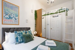 A bedroom with a bed, a nightstand, a mirror, a wardrobe, and a poster on the wall. - ^Cosy Two Bed AirCondisioned Apartment in Heart of Covent Garden London^ (London)