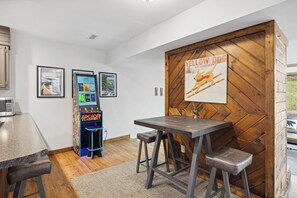 A room with a wooden wall, a table with two stools, a microwave, and arcade games.