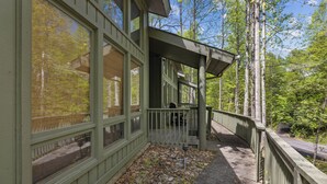A wooden deck with a stone pathway leading to a building with large windows and a green railing. - Ober Gatlinburg | Private Hot Tub | Arcade | Free High-Speed Wi-Fi (Gatlinburg)