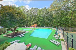 Une piscine dotée de plusieurs couloirs, entourée de gazon synthétique vert et ombragée par des parasols.