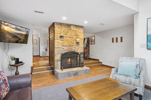 A living room with a stone fireplace, a sofa, a patterned rug, and a coffee table. - Ober Gatlinburg | Private Hot Tub | Arcade | Free High-Speed Wi-Fi (Gatlinburg)
