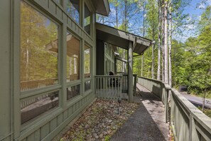 A wooden deck with a railing, a stone pathway, and a view of trees and sky.