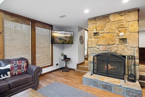 Una sala de estar con chimenea de piedra, un sofá de cuero, un televisor y una escalera que lleva a otro nivel.
