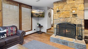 A living room with a stone fireplace, a leather sofa, and a television mounted on the wall. - Ober Gatlinburg | Private Hot Tub | Arcade | Free High-Speed Wi-Fi (Gatlinburg)