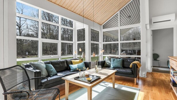 A spacious living room with large windows, a black leather sofa, a wooden coffee table, and a metal chair. - Beautiful home in Hasle with sauna (Hasle)