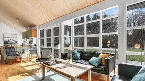 A spacious living room with a wooden ceiling, large windows, a black leather sofa, and a dining area with a wooden table and chairs. - Beautiful home in Hasle with sauna (Hasle)