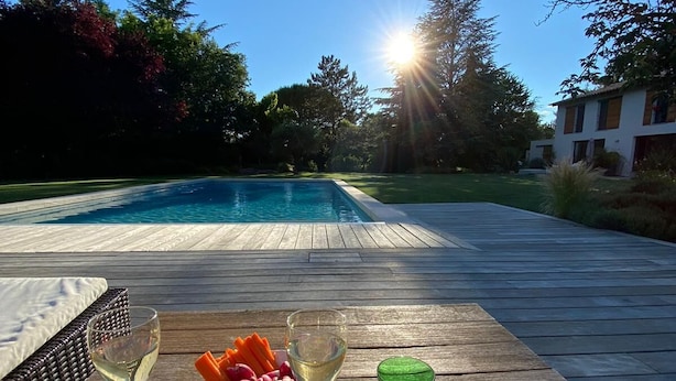 A wooden deck with a pool in the background, a glass of white wine, a bowl of fruit, and a plate of food. - Bright and Warm House, quiet, 5min from the center of Aix, (Aix-en-Provence)