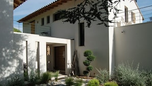 A modern house with a stone pathway leading to a wooden door, surrounded by various plants and shrubs. - Bright and Warm House, quiet, 5min from the center of Aix, (Aix-en-Provence)