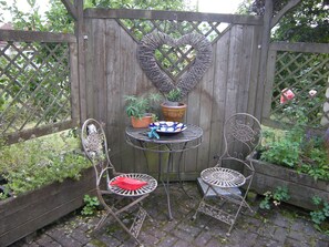 A garden patio with a heart-shaped wooden gate, two metal chairs, a small round table, and potted plants. - RHÖN-ANTIK" apartment with wood-burning stove and terrace for barbecuing. (Dipperz)
