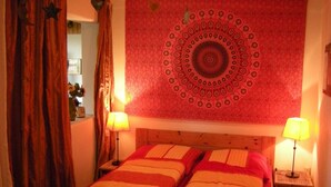 Un dormitorio con una cama de madera, dos lámparas de noche, un tapiz rojo y una araña.