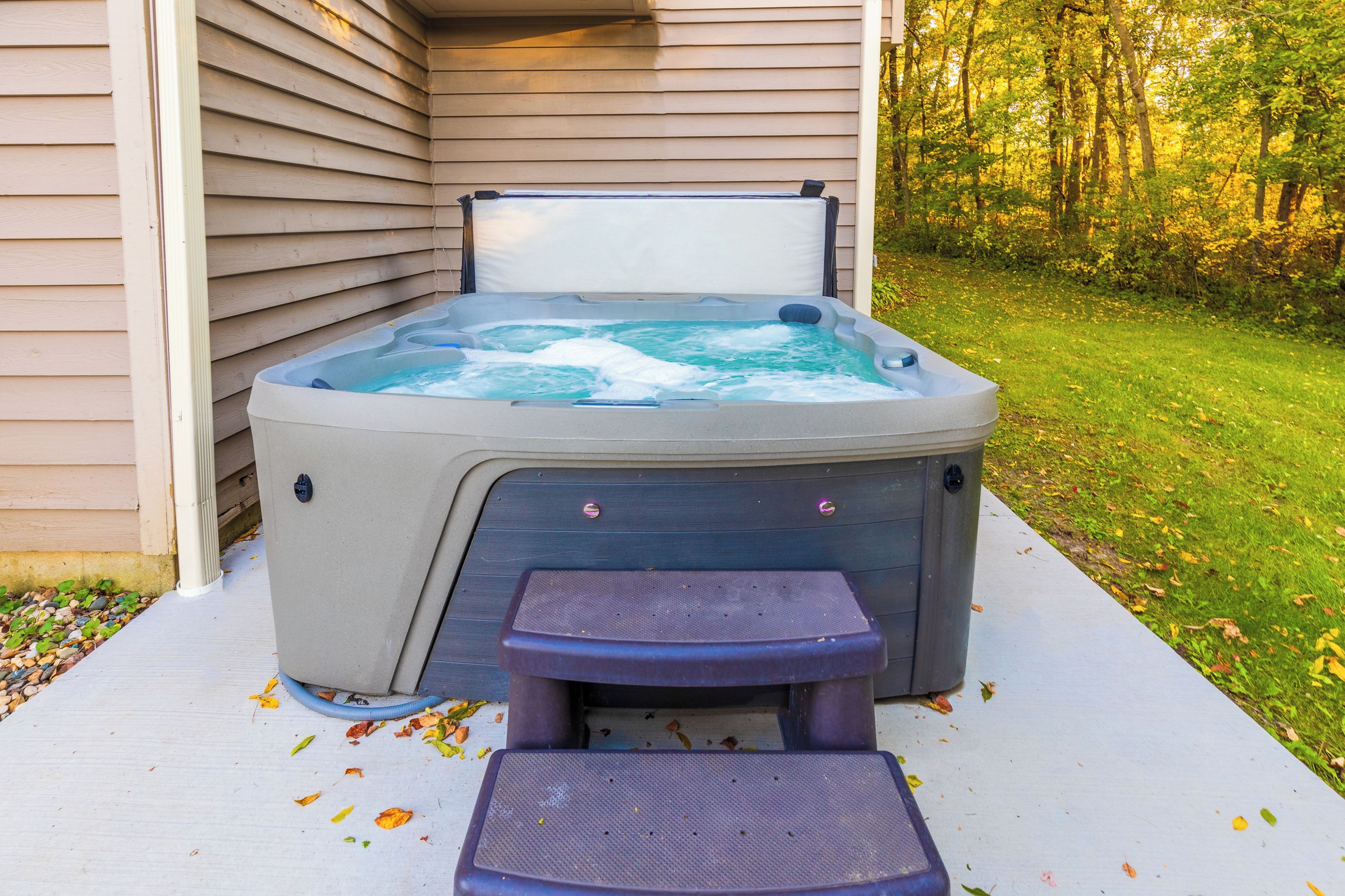 Ein Whirlpool mit integriertem Sitzplatz und Treppen, auf einer Beton-Terrasse gelegen, mit einem Holzhaus im Hintergrund.