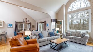 Un salon spacieux avec un plafond haut, une grande fenêtre et un coin salon confortable avec un fauteuil en cuir et des canapés.
