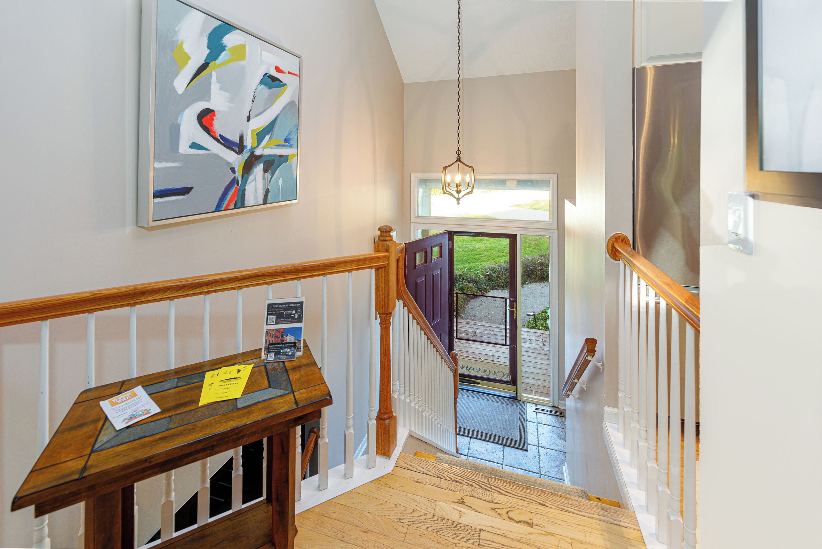 A staircase with a wooden handrail, a bench with a 'Guest Pass' sign, and a painting on the wall.