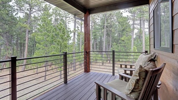 A wooden deck with a bench and a railing, overlooking a forested area. - Turkey Ridge Lodge - just outside of Deadwood! (Sturgis)