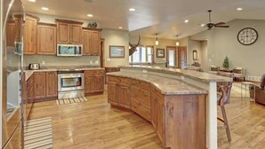 A spacious kitchen with wooden cabinets, a large island, and a ceiling fan. - Turkey Ridge Lodge - just outside of Deadwood! (Sturgis)